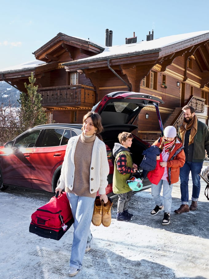 Familie mit Kindern packt Gepäck aus dem Kofferraum eines Autos vor einem Chalet im Schnee. Symbolbild für Schneeräumung in der Schweiz.