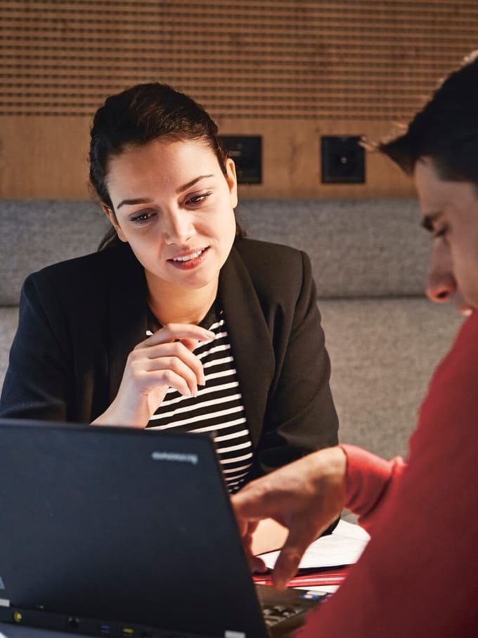 Eine Frau und ein Mann schauen auf einen Laptopbildschirm. Der Mann zeigt auf den Bildschirm. Symbolbild für Kredit und Darlehen.