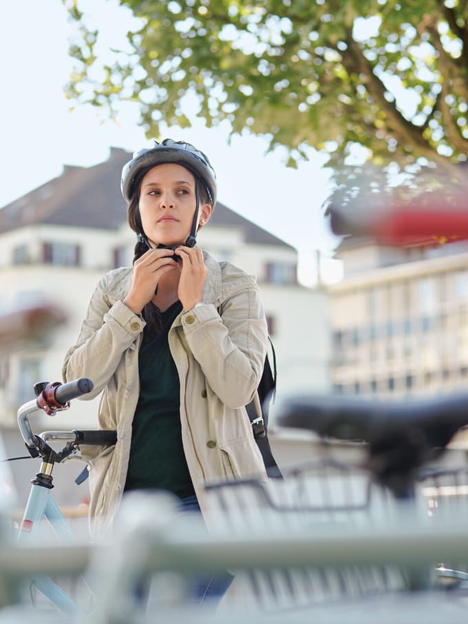 Junge Frau steht bei einem Fahrradständer und zieht ihren Helm an.