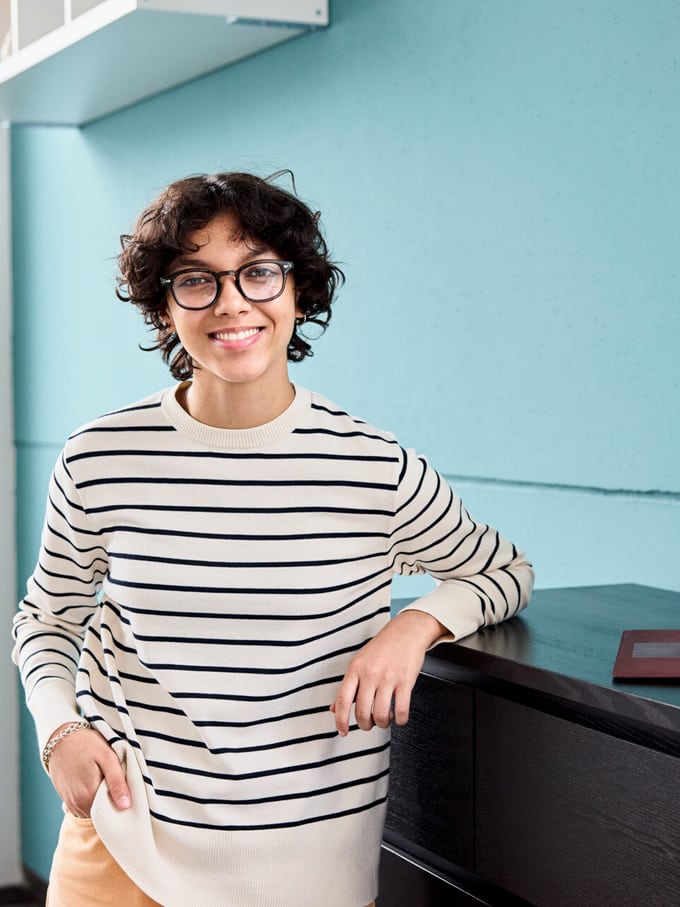 Giovane donna con gli occhiali appoggiata a un cassettone.