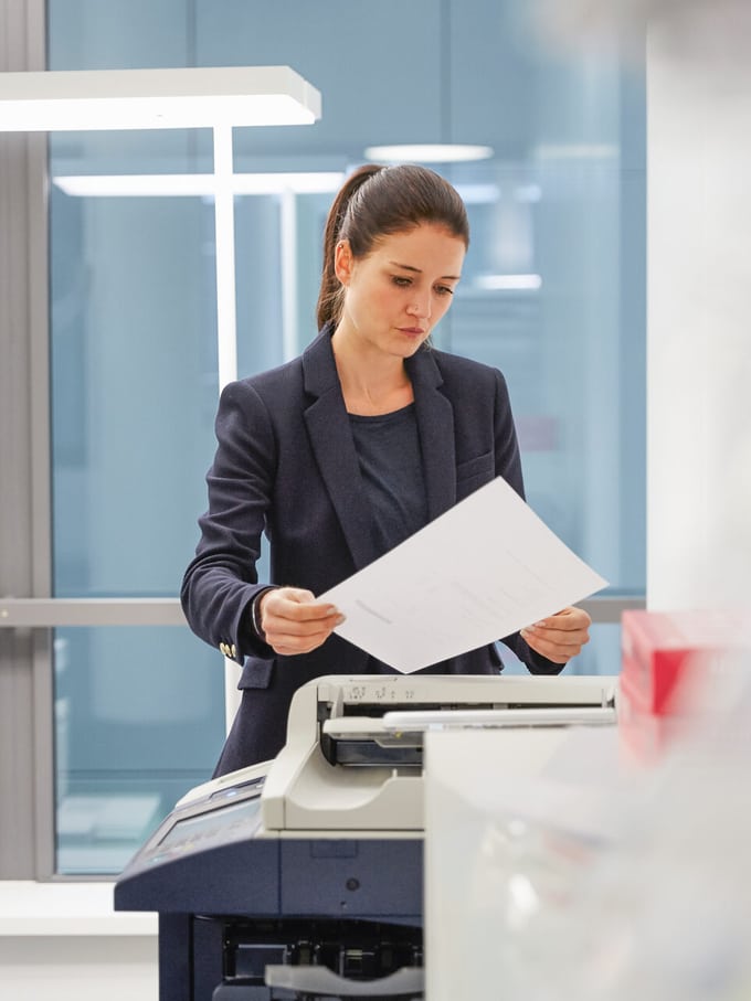Une femme en costume se tient devant une imprimante et examine, soucieuse, une lettre de congé.