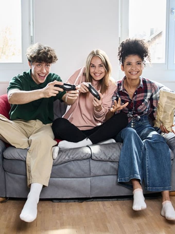 3 junge Menschen spielen auf dem Sofa Videospiele