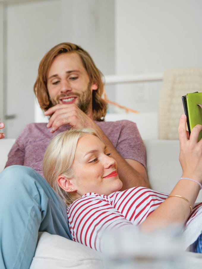 Un uomo siede sul divano, la donna appoggia la propria testa sulle sue gambe. Immagine simbolica del riconoscimento di paternità.