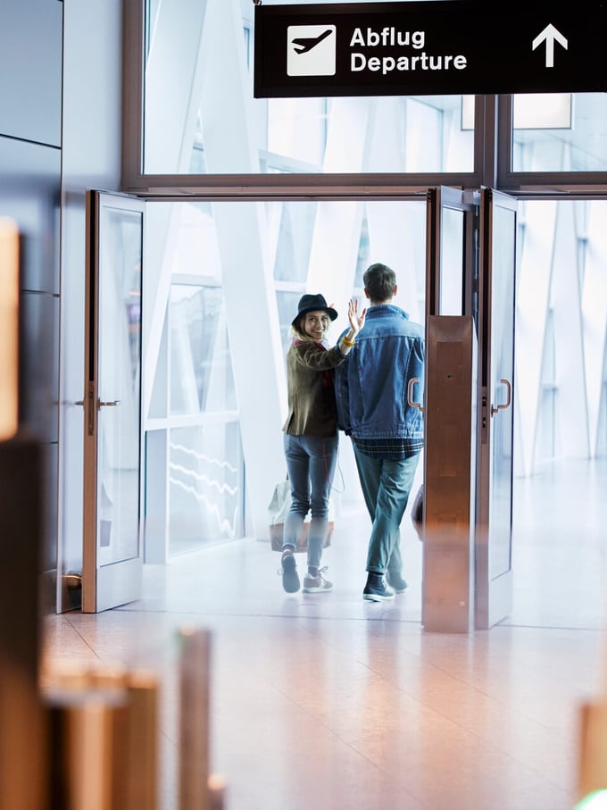 À l’aéroport, un couple se dirige vers le terminal des départs, prêt à s’envoler vers les vacances.