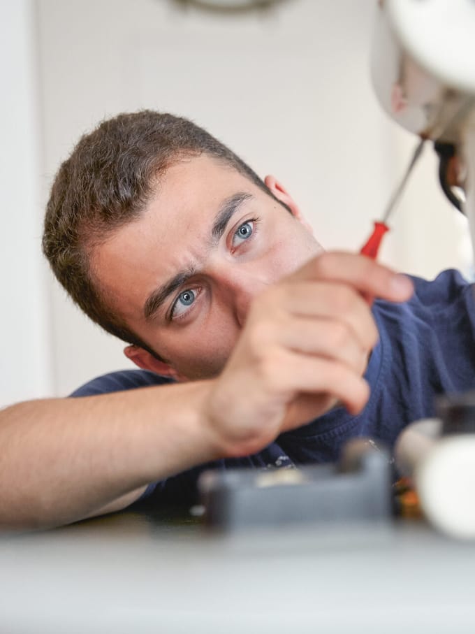 Mann repariert eine Kaffeemaschine mit einem Schraubenzieher