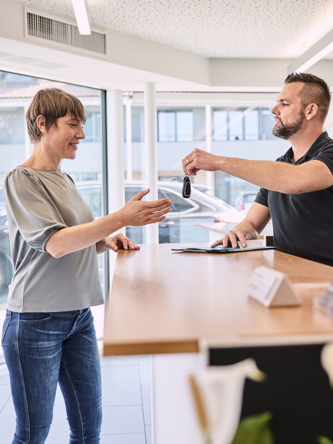 Una signora allo sportello allunga la mano per ricevere le chiavi di un’automobile. Un’immagine simbolica del noleggio di un’auto.