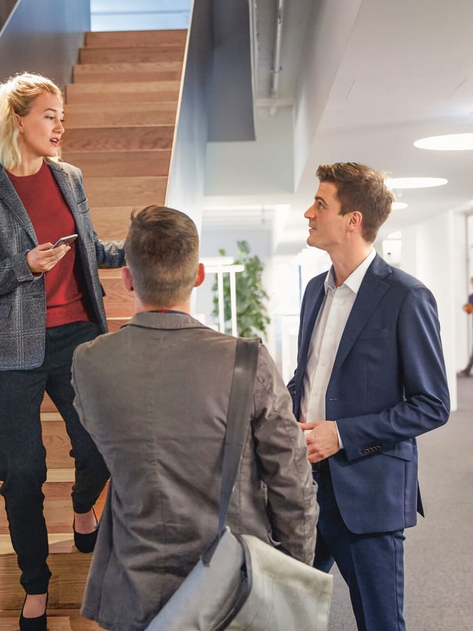 Assurance PME: une femme discute avec deux collègues de travail en tenue business dans l’escalier d’un immeuble de bureaux moderne