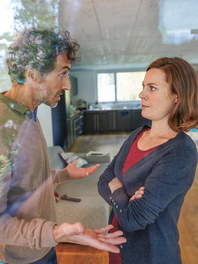 Image symbolisant le divorce et la séparation: un homme et une femme se tiennent debout face à face dans un logement. Ils ont une discussion animée. L’homme gesticule, la femme l’écoute, les bras croisés.