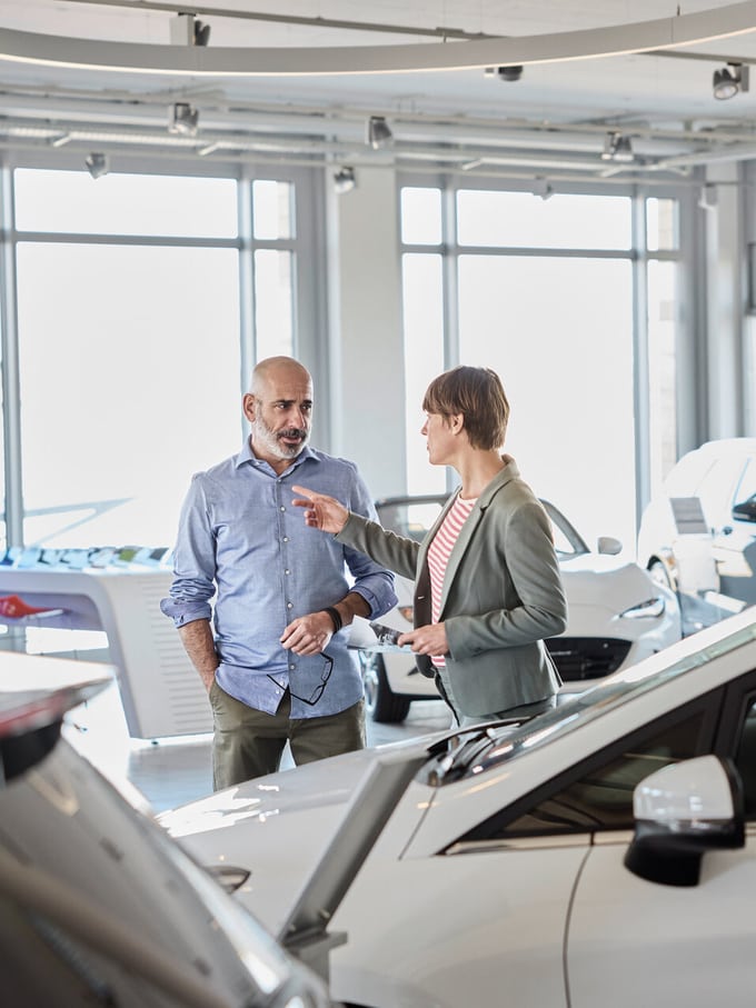 Image symbolisant le leasing automobile: un homme et une femme discutent dans le salon d’exposition d’un concessionnaire automobile.