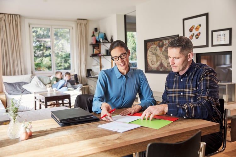 Coppie discutono i documenti al tavolo del salotto, bambini che giocano in sottofondo.   