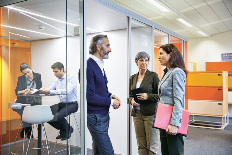 Drei Personen diskutieren im Büro vor einem Sitzungszimmer mit Glaswänden