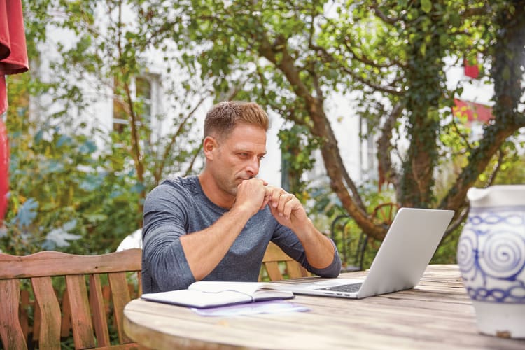 Ein Mann sitzt im Garten, vor ihm ein aufgeklappter Laptop, und recherchiert zum Thema Änderungskündigung Schweiz. 