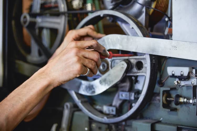 Eine Person hantiert mit einem Schraubenzieher an einer grossen Maschine. Sichtbar sind nur die Arme der Person. 