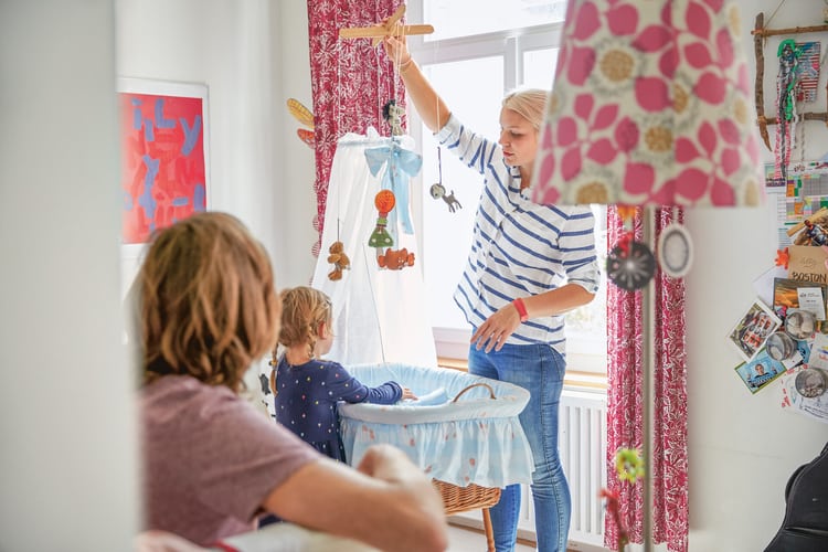 Immagine simbolica per il congedo di maternità e paternità: Due giovani genitori con un bambino piccolo sono in una cameretta davanti a una culla per neonati e la preparano per il bebè in arrivo.