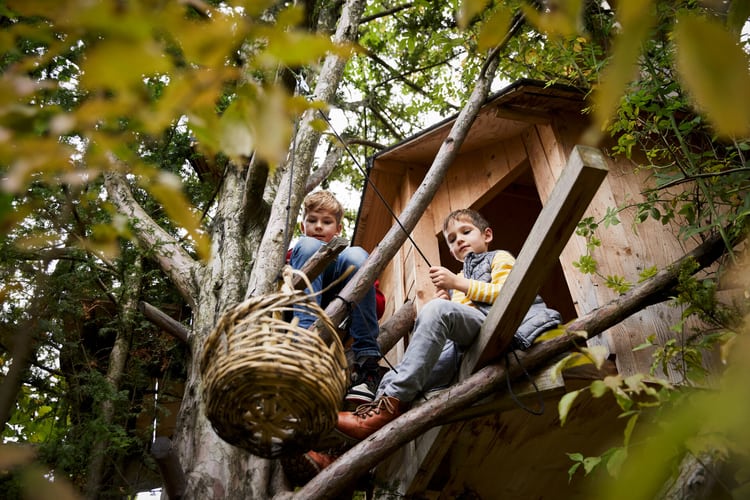 Zwei Kinder sitzen in einem Baumhaus aus Holz und spielen mit einem Seil. Sinnbild für den Ratgeber zu Licht und Schatten.