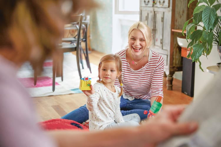Une jeune maman joue et rit avec sa fille par terre. 
