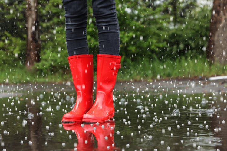 On ne voit que la partie inférieure des jambes d’un adulte qui porte des bottes en caoutchouc rouges. Les pieds sont dans une flaque et il grêle. 