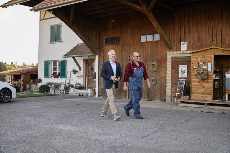 Ein Bauer und ein anderer Mann laufen über einen Bauernhof.