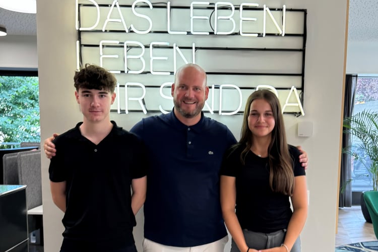 Zwei KV Lernende stehen mit dem Chef neben einander
