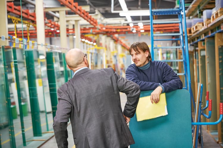 Image symbolisant la demeure: dans un hangar de travail, deux hommes se regardent. L’un d’eux tient à la main une fourre en plastique jaune.