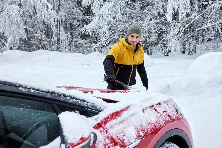 Jeune homme grattant les vitres de sa voiture en hiver 