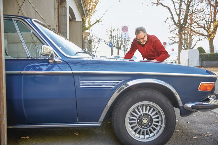 Vue latérale de la moitié avant d’un véhicule de collection dont le propriétaire lustre le capot avec soin. 