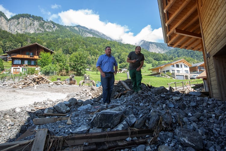 Versicherungsberater und Kunde stehen auf einem Geröllhaufen vor dem Haus, nach dem Unwetter in Brienz
