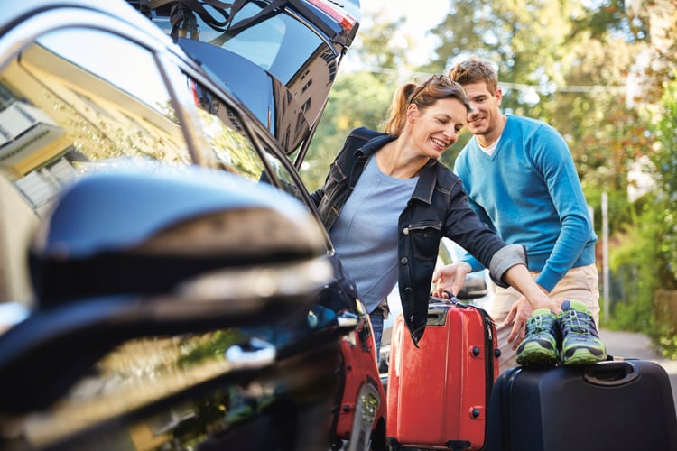 Paar packt Koffer ins Auto für eine Reise, Symbolbild für Vignette Schweiz und Mautgebühren im Ausland.