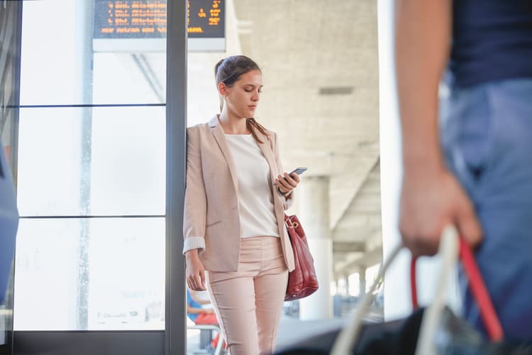 Una donna con un blazer rosa, appoggiata a una porta, guarda il suo smartphone. Immagine simbolica per la guida sul mancato pagamento del salario.