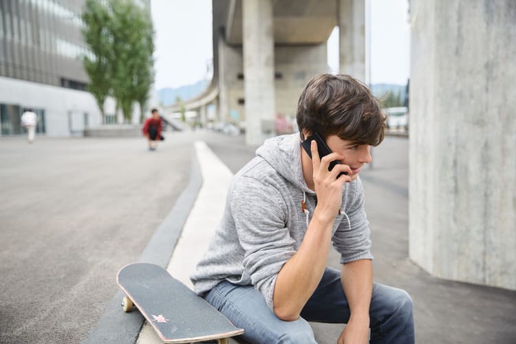 Un jeune homme est au téléphone et assis dans un escalier avec du skateboard.