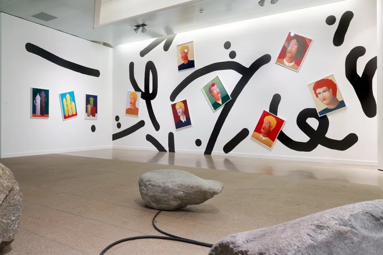 Parete con forme nere e quadri di teste all’esposizione d’arte della Mobiliare