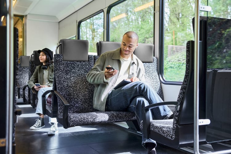 Junger Mann im Zug, hält sein Smartphone in der Hand. Er ist zufrieden.