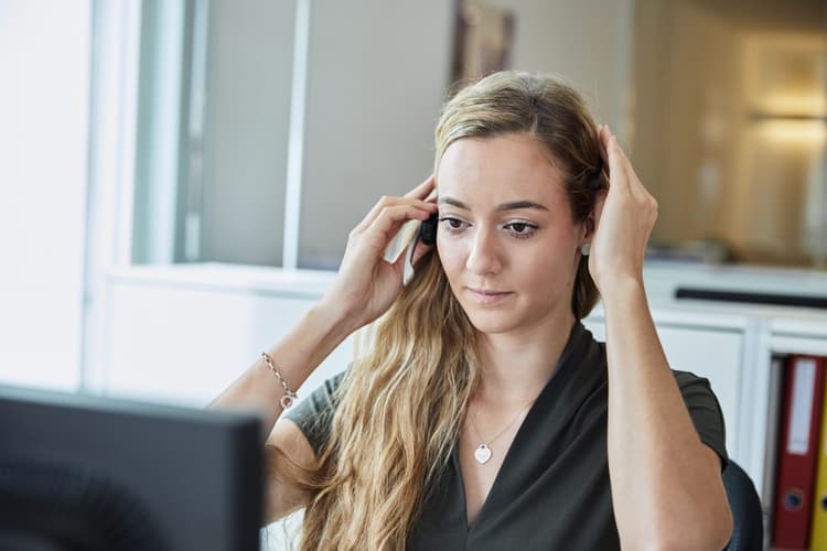 Frau sitzt vor Bildschirm und fasst sich an ihr Headset