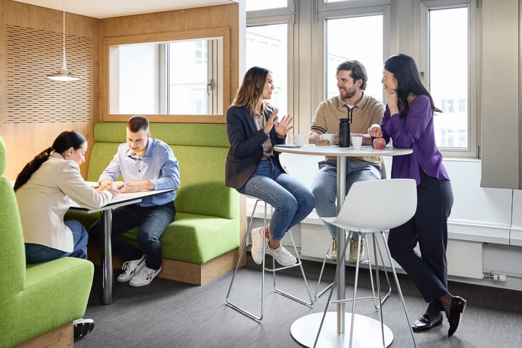 Fünf Mitarbeitende führen Unterhaltungen – drei am Stehtisch, zwei in einer Sitzecke  