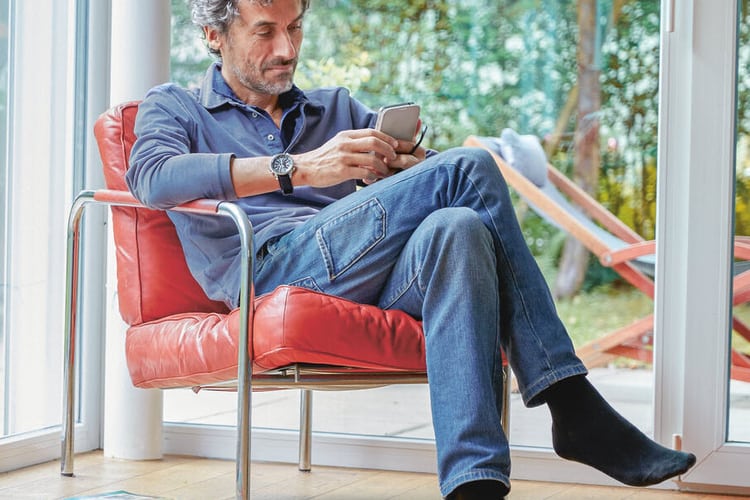 Mann sitzt mit dem Smartphone auf dem Sessel und macht ein Backup.