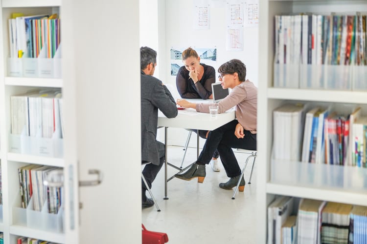 Blick in ein Büro. An einem Tisch sitzen drei Personen und besprechen etwas.