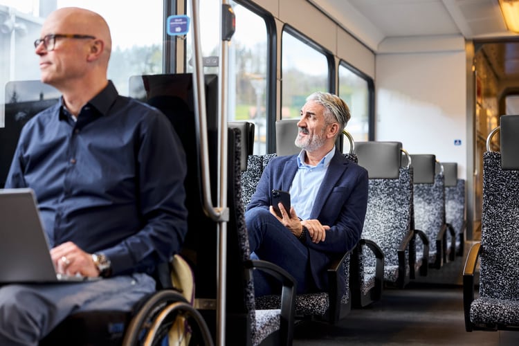 Mann im Anzug sitzt zufrieden im Zug, mit dem Smartphone in der Hand.
