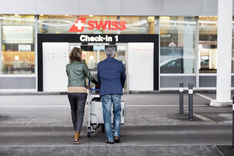 Ein Paar geht auf den Eingang des Flughafens Zürich-Airport zu, einen Kofferwagen mit dem Reisegepäck stossend. 