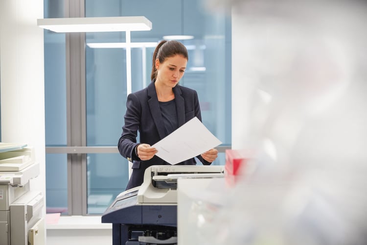 Una donna in tailleur si trova davanti a una stampante e guarda preoccupata una lettera di licenziamento.
