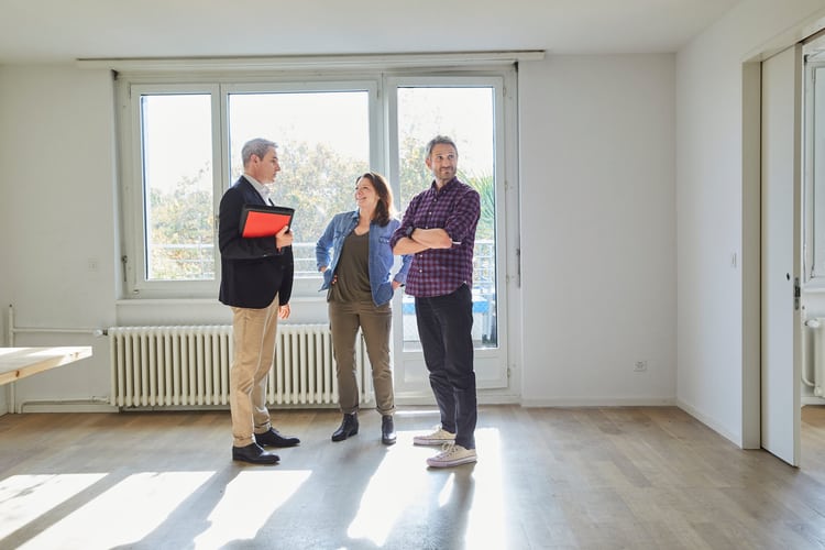 Paar im mittleren Alter mit dem Vermieter in einer leeren Wohnung als Symbolbild für Wohnungsübergabe bzw. Wohnungsabnahme.