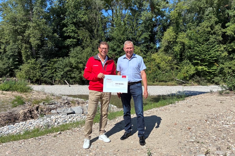 Zwei Männer stehen mit einem Check vor einem Präventionsprojekt.