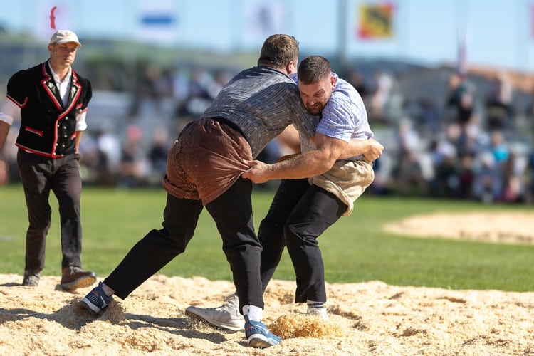 Benjamin Gapany en plein combat de lutte suisse, concentré et en prise avec son adversaire sous les yeux du juge.