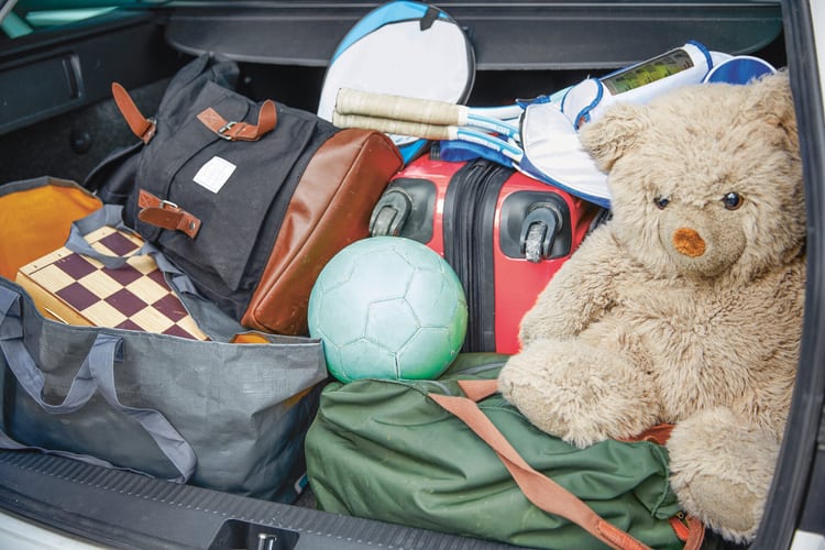Un orsacchiotto siede nel bagagliaio di un'auto, circondato da bagagli e borse da viaggio. Questa immagine simboleggia l'annullamento di un hotel o di una vacanza e le condizioni di cancellazione.