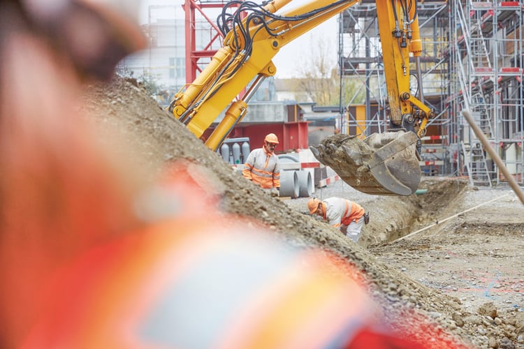 Vista di un cantiere edile con il braccio di un escavatore e due operai, come simbolo della riduzione del canone di locazione per il rumore di cantiere.
