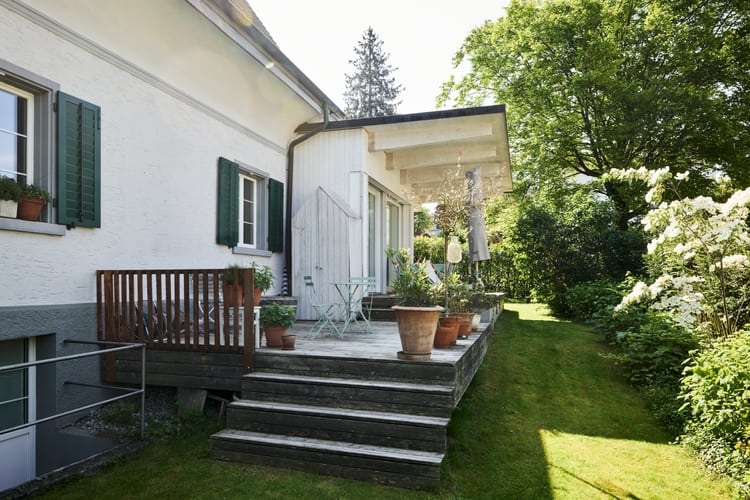 Vue latérale d’une maison dans un cadre verdoyant. Image symbolisant le thème des fenêtres non étanches dans un logement en location en Suisse.
