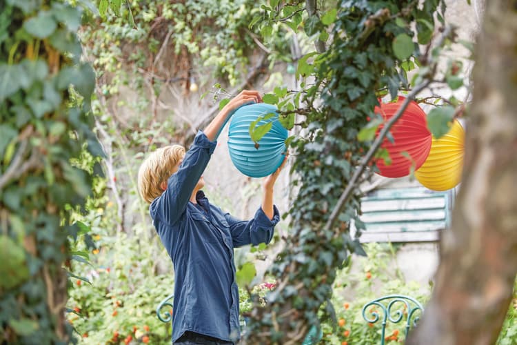 Ein Junge hängt Lampions in einen Baum.
