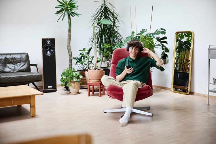 Junger Mann auf Polstersessel im Wohnzimmer mit Zimmerpflanzen im Hintergrund