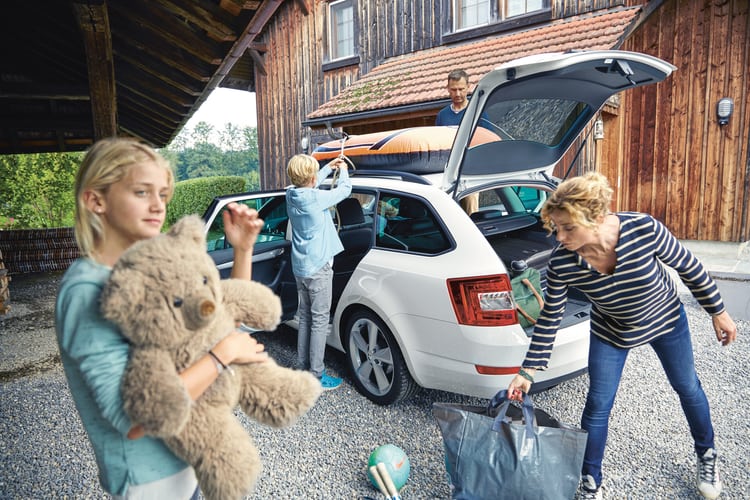 Eine Familie beladet das Auto mit dem Gepäck für die Ferien