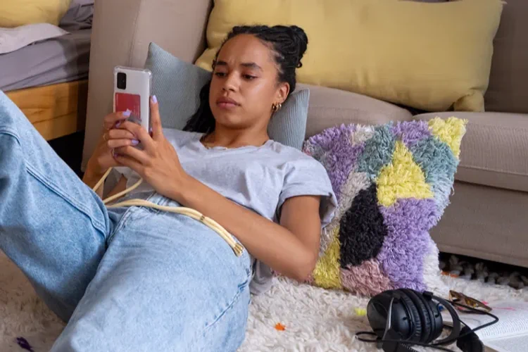 Jeune femme allongée au sol de sa chambre sur son smartphone 