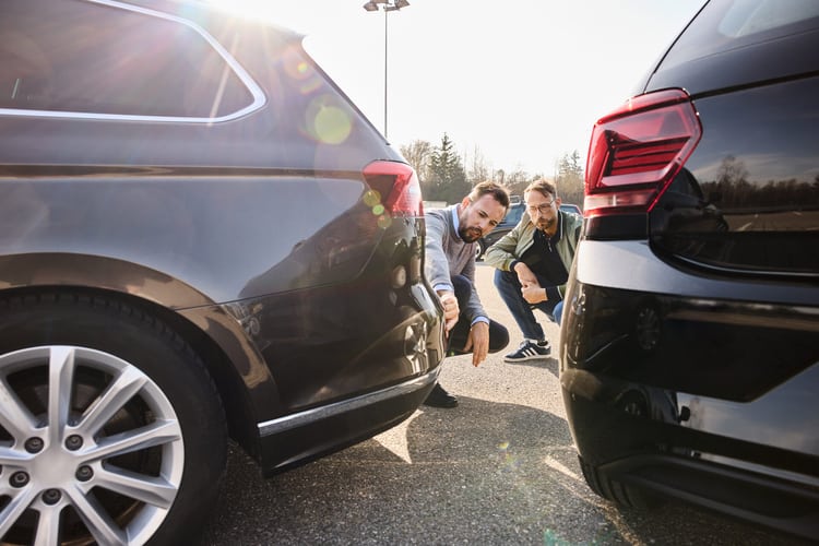 Zwei Männer knien zwischen den Heckpartien von zwei Autos und schauen sich die Schäden nach einem Zusammenstoss an. 